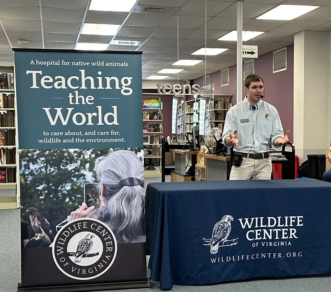 A man standing in front of a table with a blue table cloth and next to a banner that reads "Teaching the World".